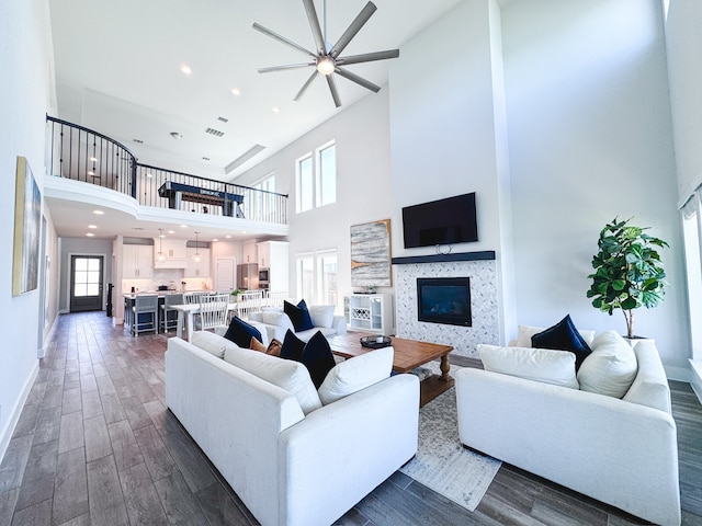 living room with ceiling fan, a fireplace, a high ceiling, and dark hardwood / wood-style floors