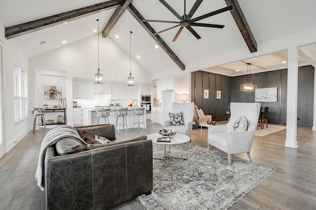 living room featuring sink, beam ceiling, light hardwood / wood-style flooring, high vaulted ceiling, and ceiling fan