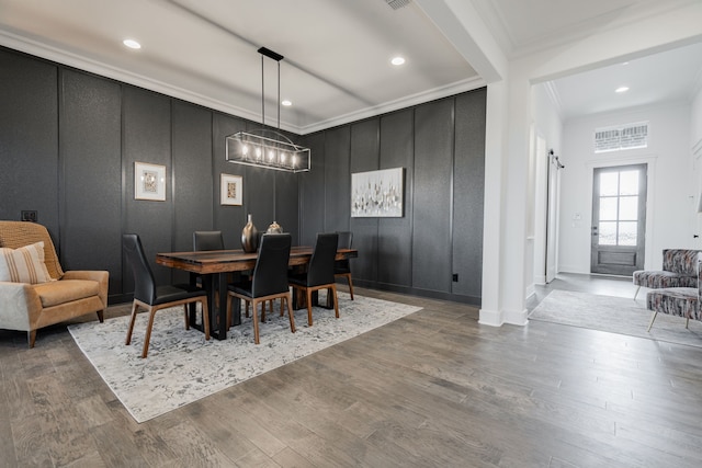 dining room with a barn door, ornamental molding, and hardwood / wood-style flooring