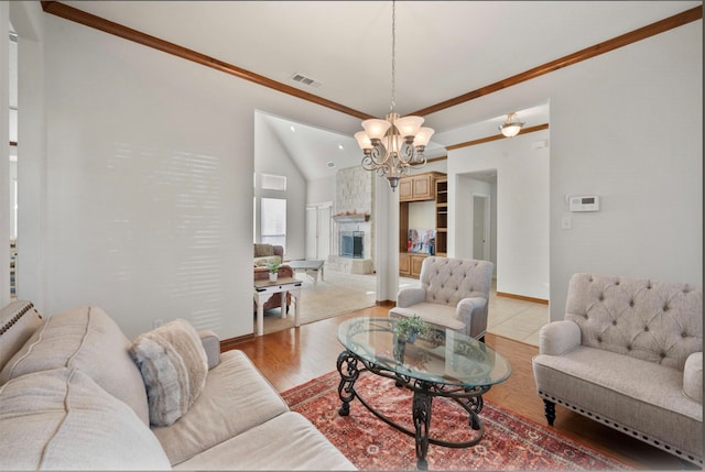 living room featuring light hardwood / wood-style floors, a stone fireplace, an inviting chandelier, crown molding, and vaulted ceiling