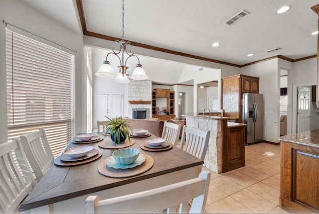 dining room featuring a textured ceiling, a fireplace, an inviting chandelier, light tile patterned floors, and crown molding