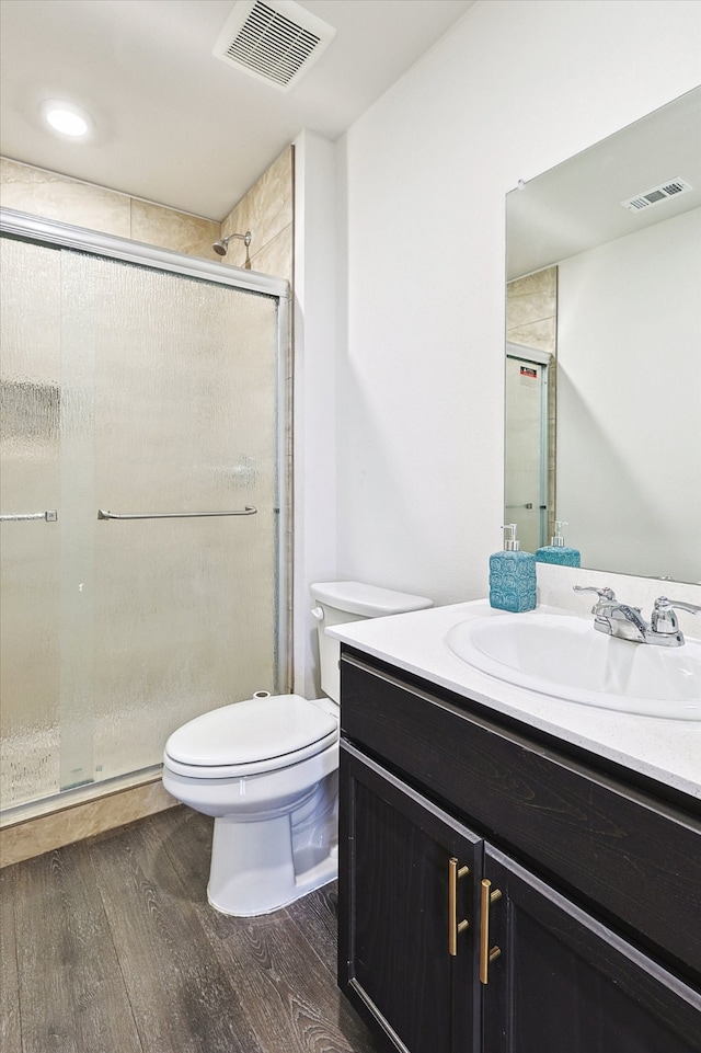 bathroom with hardwood / wood-style floors, a shower with shower door, vanity, and toilet