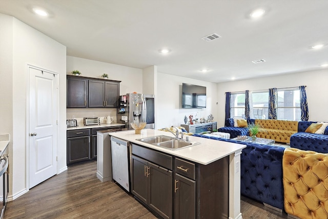 kitchen with appliances with stainless steel finishes, dark brown cabinets, a kitchen island with sink, dark hardwood / wood-style floors, and sink