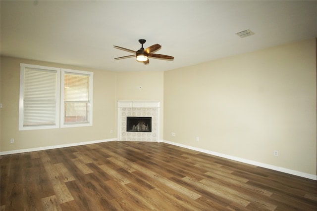 unfurnished living room with ceiling fan, dark hardwood / wood-style flooring, and a tile fireplace