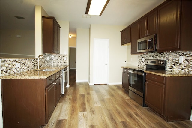 kitchen with backsplash, light stone countertops, stainless steel appliances, light wood-type flooring, and sink