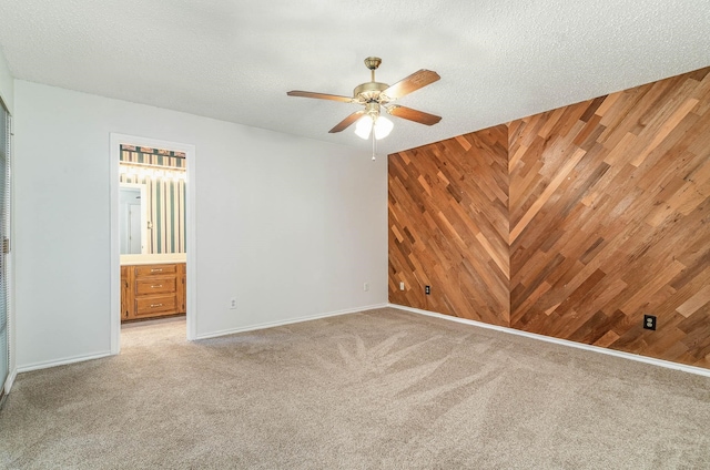 unfurnished room with carpet flooring, wooden walls, a textured ceiling, and ceiling fan