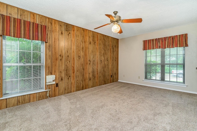 unfurnished room with wooden walls, ceiling fan, carpet flooring, and a textured ceiling