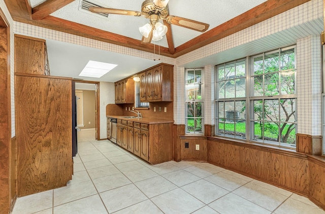 kitchen with dishwasher, light tile patterned floors, ceiling fan, a skylight, and sink