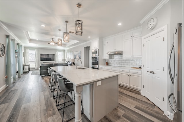 kitchen with stainless steel appliances, hardwood / wood-style floors, an island with sink, a breakfast bar, and white cabinetry