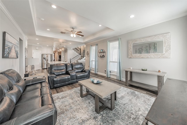 living area with ceiling fan with notable chandelier, wood finished floors, stairs, and a raised ceiling