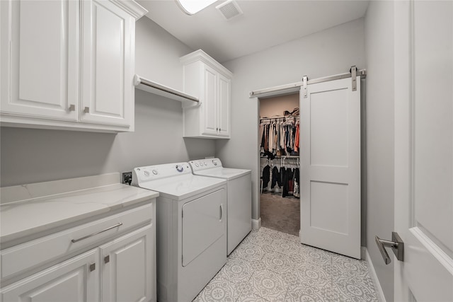 clothes washing area featuring cabinets, a barn door, and separate washer and dryer