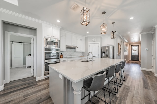 kitchen featuring stainless steel appliances, a barn door, sink, white cabinets, and a spacious island