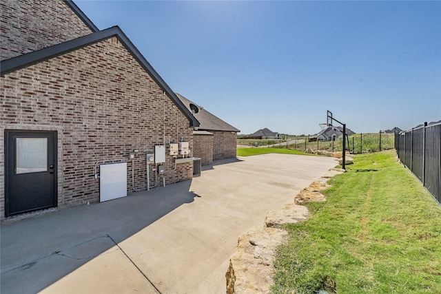 view of side of property with central air condition unit, fence, a yard, a patio, and brick siding