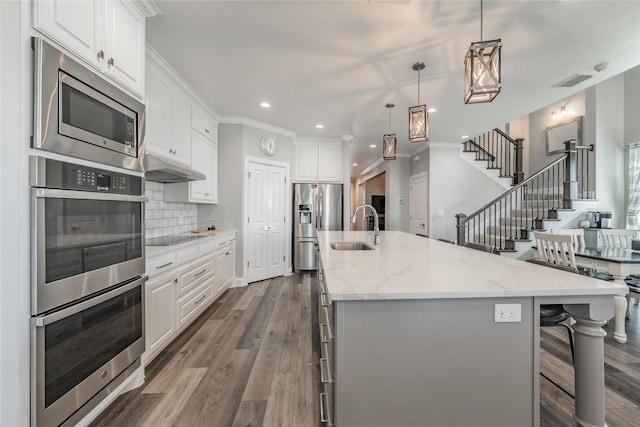 kitchen featuring a sink, white cabinets, stainless steel appliances, a center island with sink, and dark wood finished floors