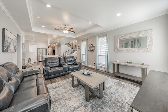 living room with hardwood / wood-style flooring, ceiling fan, ornamental molding, and a tray ceiling