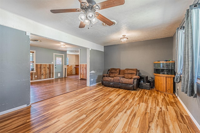 living room featuring a textured ceiling, ceiling fan, light hardwood / wood-style floors, and wooden walls