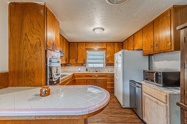 kitchen featuring kitchen peninsula, sink, appliances with stainless steel finishes, a textured ceiling, and tile counters