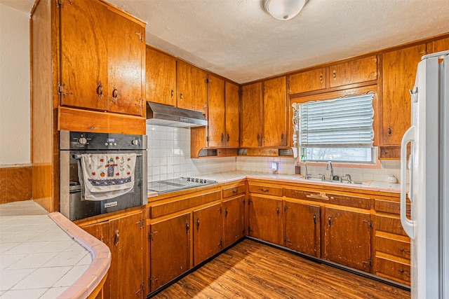 kitchen with hardwood / wood-style floors, black electric stovetop, white fridge, decorative backsplash, and oven