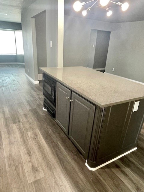 kitchen featuring black microwave, hardwood / wood-style floors, light stone counters, and dark brown cabinetry