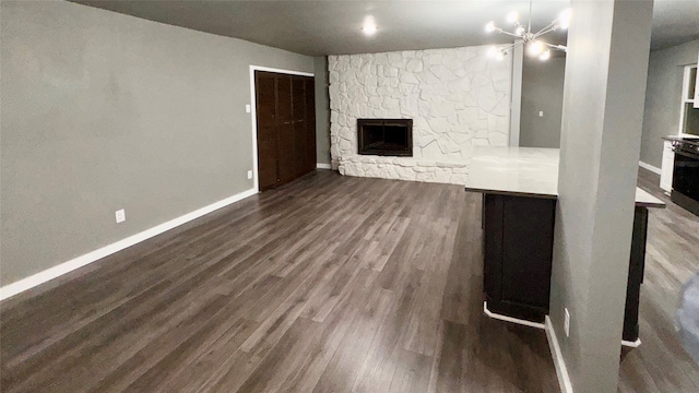 unfurnished living room with a fireplace, a chandelier, and dark wood-type flooring