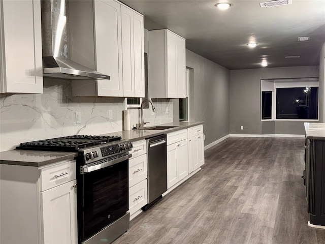 kitchen featuring wall chimney range hood, sink, stainless steel appliances, and white cabinets