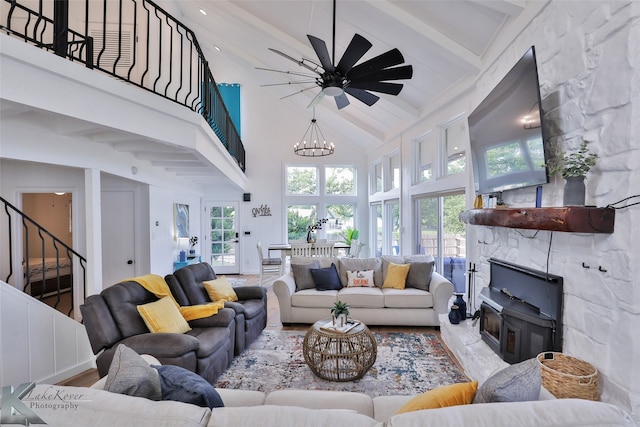 living room with high vaulted ceiling, ceiling fan with notable chandelier, a stone fireplace, beamed ceiling, and hardwood / wood-style flooring