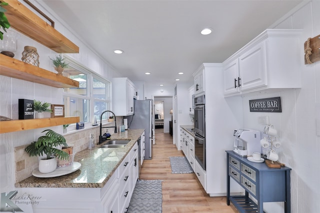 kitchen with light wood-type flooring, light stone counters, sink, white cabinetry, and decorative backsplash