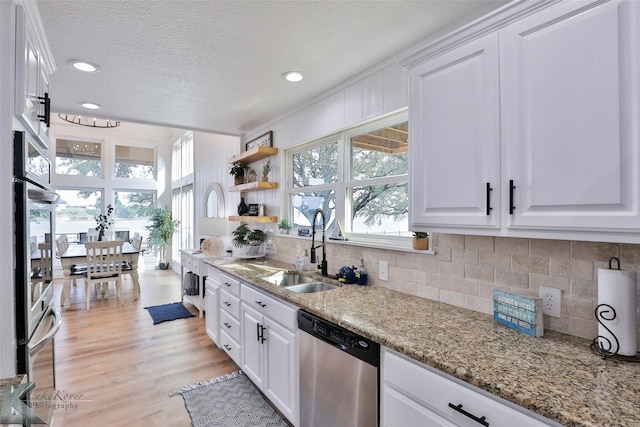 kitchen featuring light hardwood / wood-style floors, white cabinetry, light stone counters, stainless steel dishwasher, and sink