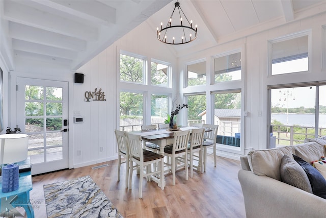 dining room featuring beam ceiling, light hardwood / wood-style flooring, a towering ceiling, a water view, and an inviting chandelier