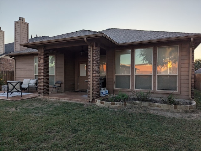 back house at dusk featuring a yard and a patio area