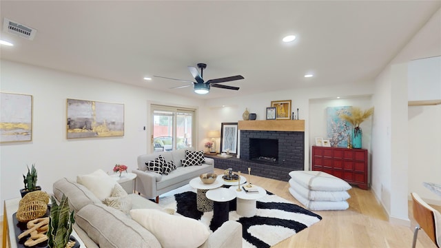 living area featuring light wood finished floors, visible vents, a ceiling fan, a brick fireplace, and recessed lighting