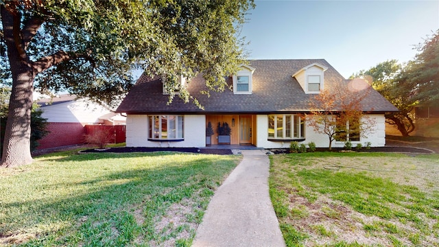 cape cod home with roof with shingles, brick siding, fence, and a front lawn