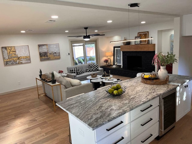 kitchen featuring beverage cooler, white cabinetry, open floor plan, hanging light fixtures, and light stone countertops