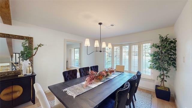 dining room with light wood-type flooring, a chandelier, and beamed ceiling