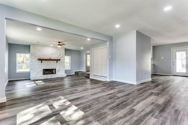 unfurnished living room featuring ceiling fan, dark hardwood / wood-style floors, and a stone fireplace