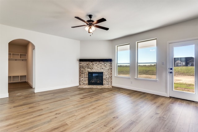 unfurnished living room featuring light wood finished floors, a fireplace, baseboards, and a ceiling fan