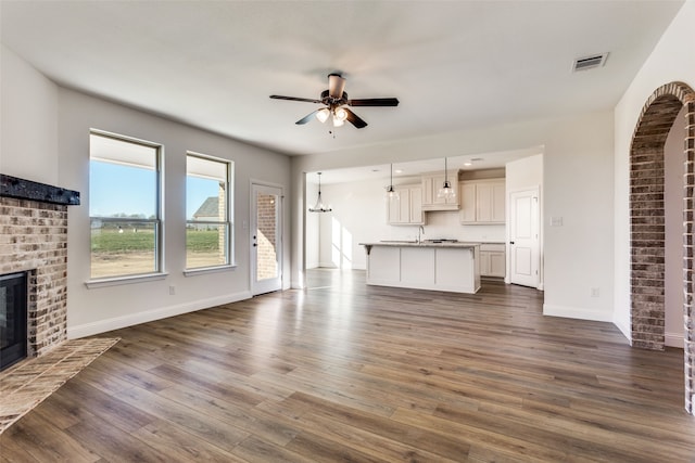 unfurnished living room featuring visible vents, dark wood-type flooring, a brick fireplace, ceiling fan, and baseboards