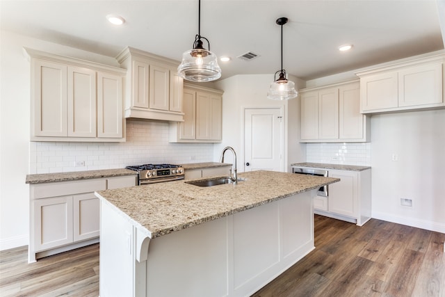 kitchen featuring an island with sink, hanging light fixtures, sink, stainless steel range, and hardwood / wood-style floors