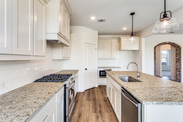 kitchen featuring appliances with stainless steel finishes, pendant lighting, light hardwood / wood-style flooring, a kitchen island with sink, and sink