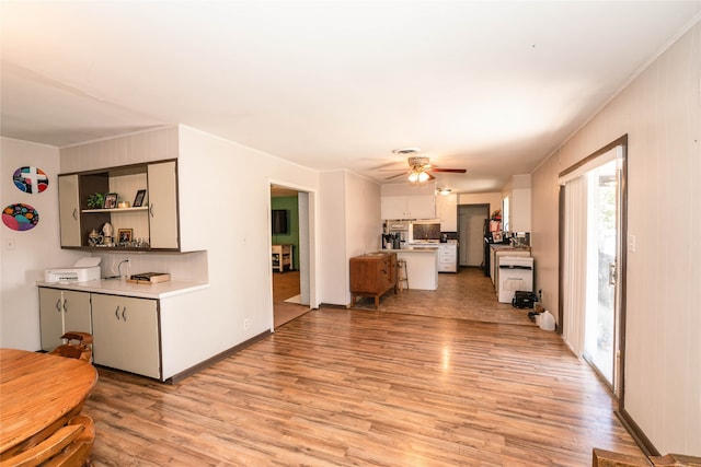 kitchen with light wood-type flooring, ornamental molding, white cabinetry, and ceiling fan