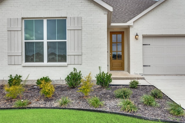 view of exterior entry with a shingled roof, brick siding, and an attached garage