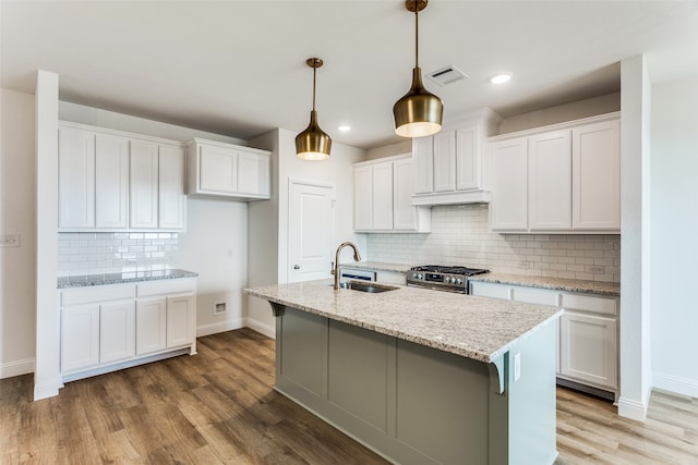 kitchen with a sink, white cabinets, stainless steel gas range, light stone countertops, and pendant lighting