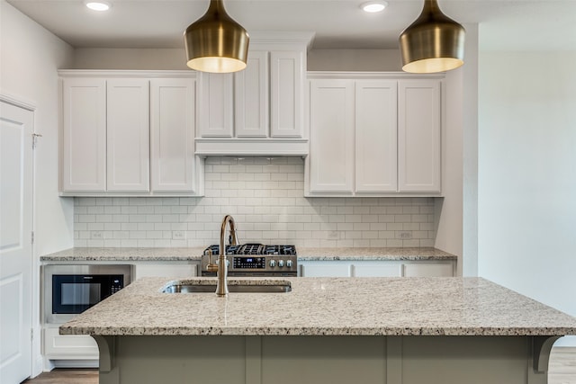 kitchen with light stone counters, a breakfast bar area, a sink, white cabinets, and tasteful backsplash