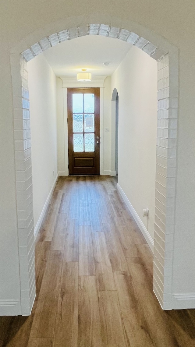 doorway to outside with arched walkways, light wood-type flooring, and baseboards