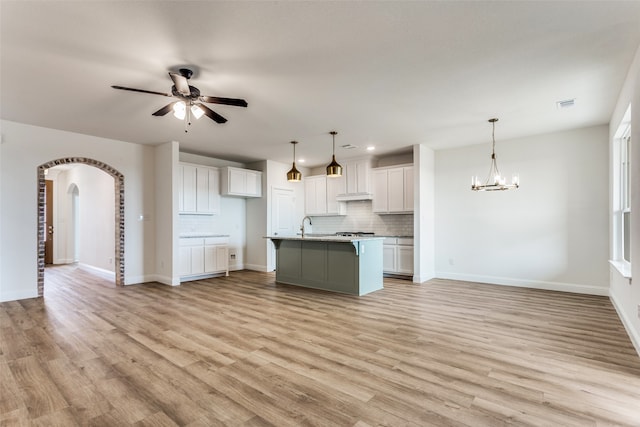 kitchen featuring arched walkways, visible vents, hanging light fixtures, tasteful backsplash, and a center island with sink