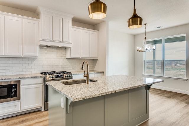 kitchen with pendant lighting, a kitchen island with sink, white cabinetry, stainless steel gas range, and under cabinet range hood