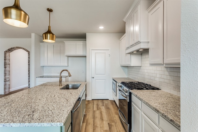 kitchen featuring a sink, white cabinetry, appliances with stainless steel finishes, an island with sink, and decorative light fixtures