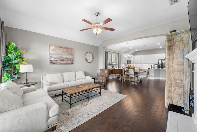 living room with a tile fireplace, ceiling fan with notable chandelier, and dark wood-type flooring