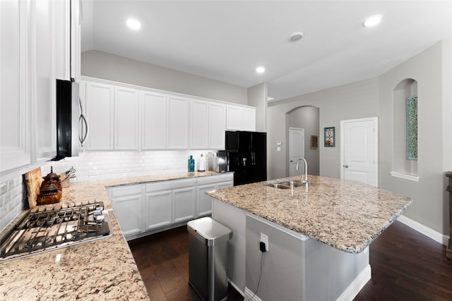 kitchen with an island with sink, white cabinetry, appliances with stainless steel finishes, dark hardwood / wood-style flooring, and light stone countertops