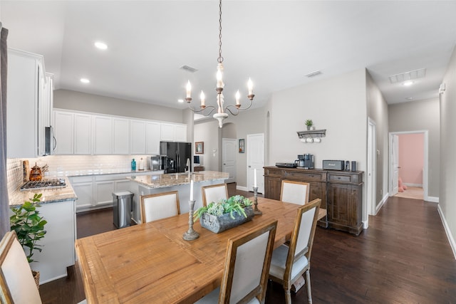 dining space featuring sink, dark wood-type flooring, and a notable chandelier